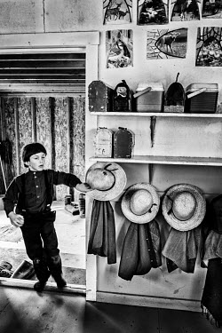 An Amish boy hangs his straw hat on a peg as he entering a classroom at his school.