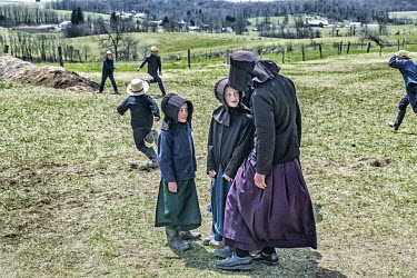 Amish schoolgirls talking while boys play a 'hit and run' game in the playingfields around the school.