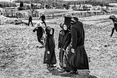 Amish schoolgirls talking while boys play a 'hit and run' game in the playingfields around the school.