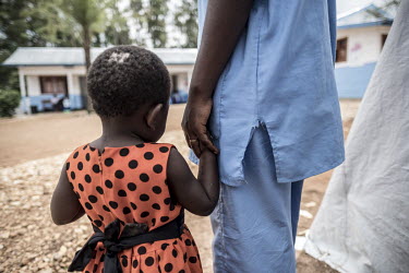 A nurse, and Ebola survivor, holds the hand of a young girl whose parents are in the adjacent Ebola treatment centre.