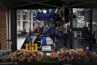 People have their hair cuts in a barber's shop behind a busy market stall which sells both British grown and imported produce.