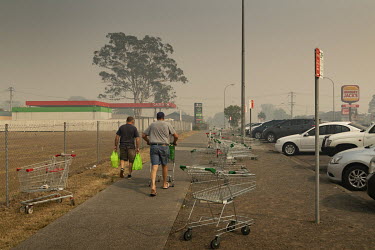 Two men walk through heavy smoke from bushfires with their shopping. Taree is at risk of being destroyed by fire, as weather conditions in New South Wales (NSW) have made circumstances ideal to spread...