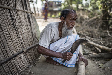 Abdul Khader, who has been blind since childhood, cuts a length of bamboo with a machete at a building site in his compound.
