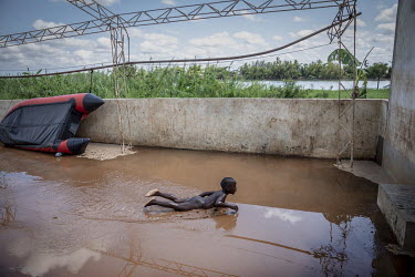 A boy from a family who stayed in the village swimming in a shallow pool of water left behind on the concrete floor after a rain shower. Most families left the village after the Pungwe River broke its...