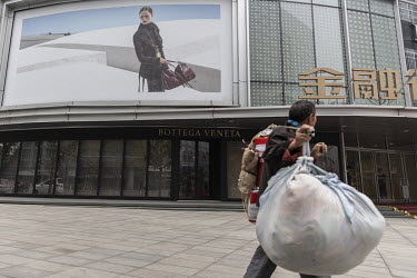 A man carrying large bundles of recyclable scraps walks past a luxury boutique.