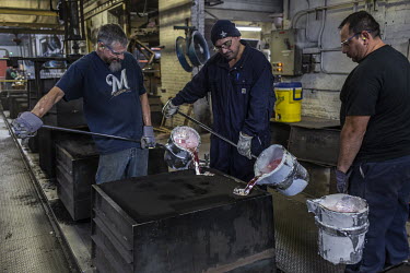 Employees Ace Waak (L), Robert Flores (centre) and Marcos Alfaro pour molten aluminum, at 760 Celsius, that will be made into an engine housing component at the Wisconsin Aluminum Foundry. The factory...