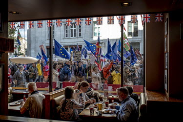 People march past diners having a meal in a cafe in London during a rally in favour of another referendum on Brexit.