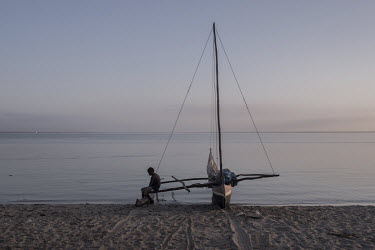 A boy sits on an outrigger fishing boat moored on the beach.