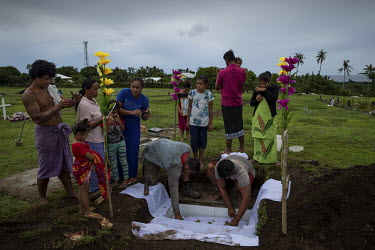Family of nine month old Mark Itaifafo place flowers on the child's coffin during his funeral at Vailele Cemetery. Other family film the service as it is common for funerals to be lived-streamed on Fa...
