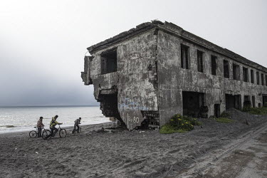 Teenagers riding bicycles on the beach next to the destroyed apartment blocks of the so called 2nd Base, an area of Oktyabrsky Settlement that is heavily affected by coastal erosion. Since the 1970s t...