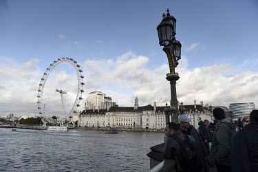 Tourists admire the view from Westminster Bridge with the London Eye to their right.