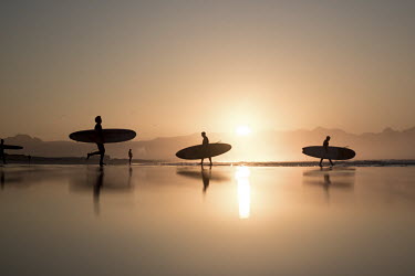 Surfers walk across Muizenberg beach at dawn.