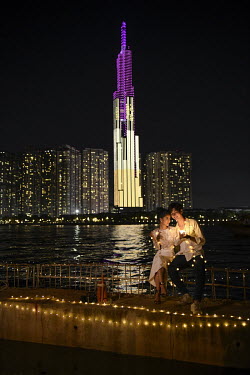 A couple pose for a photograph near Landmark 81, a high rise residential tower illuminated at night in the city centre.