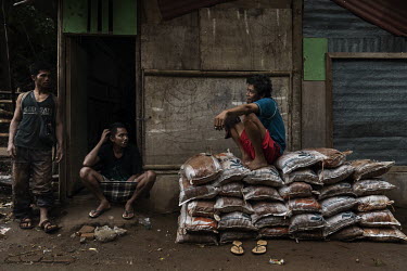 A worker at a ball mill resting with colleagues sits on a stack of ore filled sacks that have been carried down a mountainside by porters from a small-scale artisanal gold mine on the Indotan concessi...