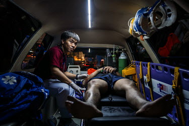 A paramedic stabilises a drunk motorbike rider in the back of an ambulance after he crashed, during Songkran festivities, when there is a spike in traffic accidents.