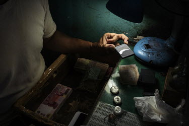 Tamhid (44), a gold dealer, checks the concentration and quality of gold from a small-scale, artisanal gold miner, who uses mercury to extract gold from the ore, in his gold shop.