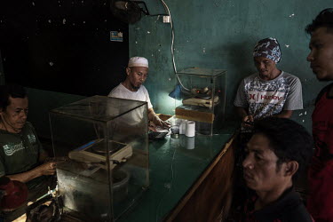 Tamhid (44) (2nd from left), a gold dealer, calculates the price, which is based on the concentration and quality of a gold nugget supplied from a small-scale, artisanal gold miner (right), who uses m...