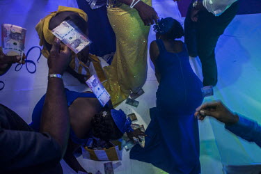 A man scatters 100 Niara notes, which are retrieved on behalf of the newly wed couple, a tradition retained at the wedding of a wealthy couple.