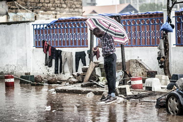 During the rainy season, a man holding an umbrella stands on a lump of concrete rising just above the water level on a flooded street.