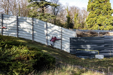A woman looks through metal barriers running through the UN's Palais des Nations park to keep the construction site separate, but making pedestrian movement through the park complicated. The Strategic...