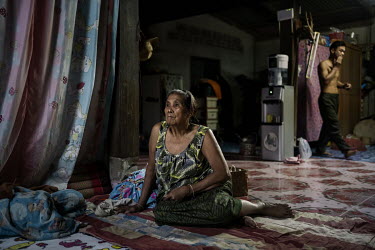 Aumka Chanlong (68) watches TV as her son in law, Wittaya Thongnetr (48) walks behind her in the home they live in close to the Mekong River.
