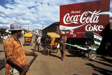Rickshaw pullers stand beside a hand painted advertisement for Coca-Cola.