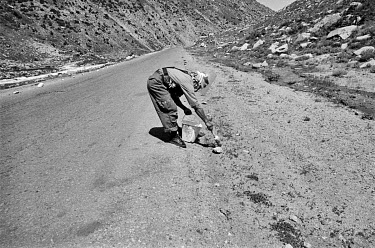 A member of a landmine clearing squad paints stones lining a road with white paint to mark the location of an area contaminated with landmines.