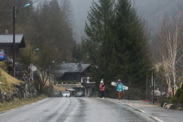 Snowboarders walking along a road, with no snow, outside the resort of Morzine.