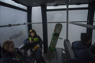 A snowboarder travelling down the mountain in a cable car looking at his mobile phone as darkness falls at the end of the day in the ski resort of Avoriaz. Despite being less exposed than many other r...