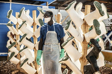 A staff member responsible for washing and disinfecting personal protective equipment (PPE) stands beside a stand used for drying rubber boots at the Ebola Treatment Centre (CTE).