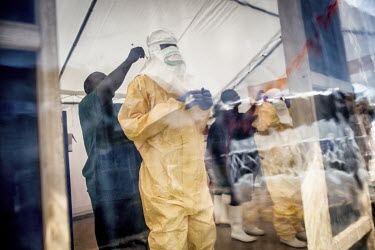 A medical team, preparing to enter the high-risk area of the Ebola Treatment Centre CTE, are helped by colleagues into their personal protective equipment (PPE).
