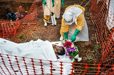 Health workers dressed in full personal protective equipment (PPE) place some artificial flowers beside the body of Finda Marie Kamano (33) who died just two days after being brought to the Ebola Trea...