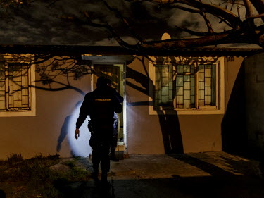 A policeman approaches a house where suspected criminals are thought to be.   Bonteheuwel neighborhood is a densely populated shanty towns (or townships) mostly inhabited by poor black and 'coloureds...