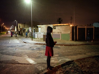 A girls stands on a street corner at night in Bonteheuwel.  Bonteheuwel neighborhood is a densely populated shanty towns (or townships) mostly inhabited by poor black and 'coloureds'.