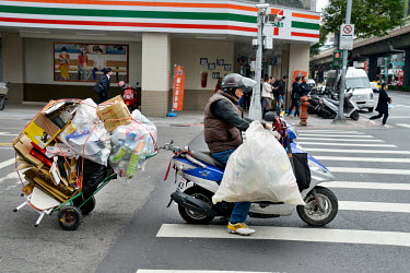 An elderly man collecting rubbish for recycling carried on a trolly pulled behind his motor scooter.