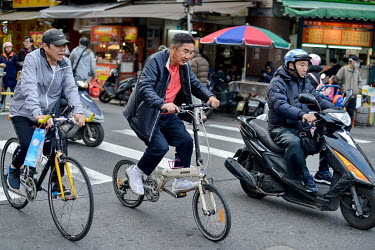 Cyclists and a scooter rider travel along a crowded street in the historic Wanhua District.