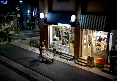 A scrapman pushes his cart past the illuminated window of a high-end fashion store in the area around Chifeng Street.