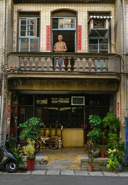 The occupant of a traditional shophouse looks out from his balcony, in a lane off of Chifeng Sreet.