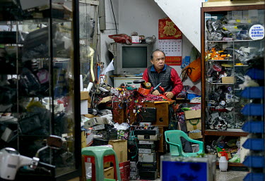 The owner surrounded by piles of old devices inside an electronics workshop on Chifeng Street.