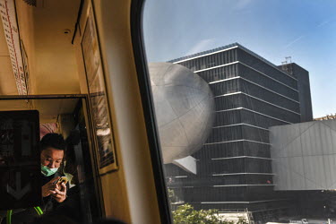 A metro passenger looks at his smartphone whilst travelling past the iconic Taipei Performing Arts Centre.