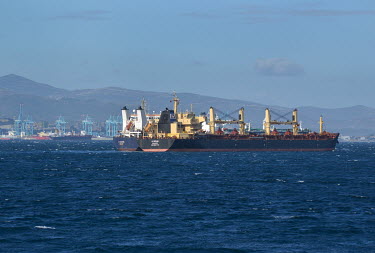 Cargo ships moored off the coast of Gibraltar with mainland Spain in the distance.