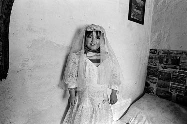 A Roma girl dressed in communion dress poses for a photo in her apartment.