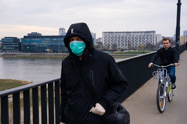 A man wearing a face mask walking on the Poniatowski Bridge, over the Vistula River.