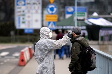 A Polish border and health patrol guard with a protective face mask and hazmat suit checks the body temperature of people crossing the border as coronavirus containment efforts are enforced on the Ode...