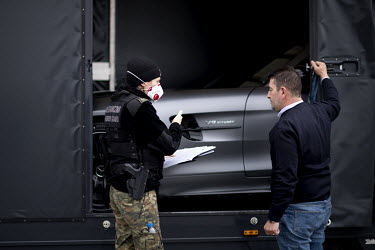 A Polish border and health patrol guard, with a protective face mask, questions a driver about his importation of a luxury vehicle as coronavirus containment efforts are enforced on the Oder Bridge, t...