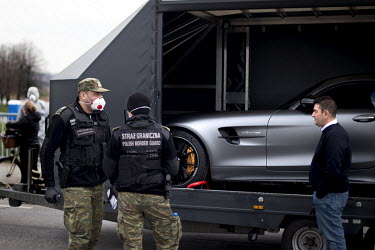A Polish border and health patrol guard, with a protective face mask, questions a driver about his importation of a luxury vehicle as coronavirus containment efforts are enforced on the Oder Bridge, t...