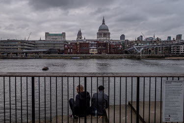 Two men sit beside the River Thames. On the opposite bank is the City of London School with St Paul's Cathedral risng behind. The UK is in lockdown, in response to the coronavirus, and the government...