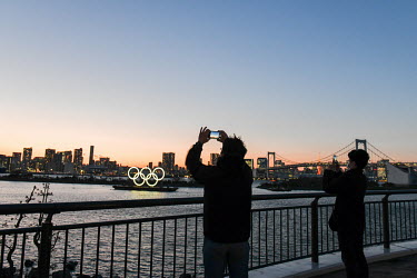 People take pictures on the waterside in Tokyo Bay of a barge displaying illuminated Olympic Rings. It has been announced that, due to the coronavirus crisis, the games will be postponed until 23 July...