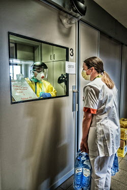 Medical staff working in an intensive care isolation ward at the Jessa hospital communicate with hand written notes with a nurse outside the room who is carrying water for staff outside.
