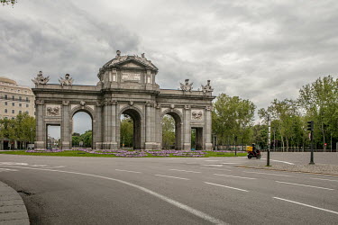 A lone motor scooter delivery driver passes the triumphal arch (Puerta de Alcala) at Alcala Street, usually a very busy spot, but nearly empty during the confinement imposed by the state of alert decl...